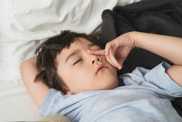 Toddler boy rubbing eyes,Kid wearing pajamas laying down on bed,Kid waking up in with unhappy face