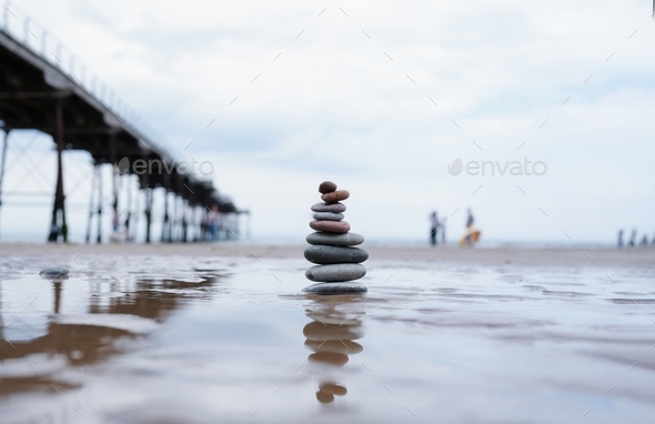 Pebble tower by seaside with blurry pier down to the sea, Stack of Zen rock stones on the sand,