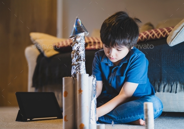 Schoolkid making spaceship for his homework, Happy child boy sitting on the floor playing with rocke