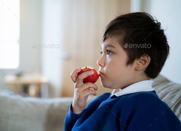 Mixed race child eating red apple while watching TV,Side view cute boy eating fresh fruit for snack - Stock Photo - Images