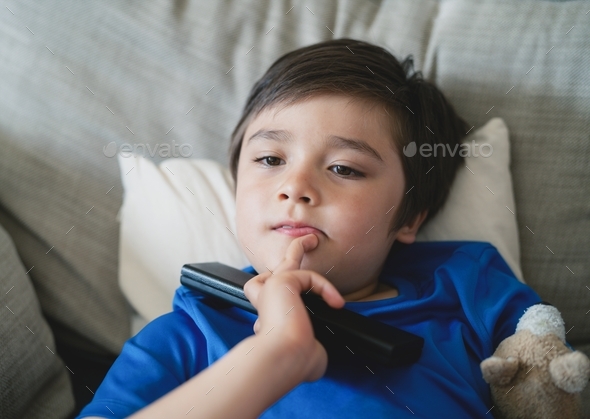Mixed race boy lying on sofa watching cartoon on Tv,SchoolKid holding remote control,Child relaxing