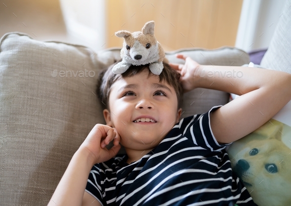 Smiling boy lying on sofa playing with dog toy,Kid having fun with his toys in living room