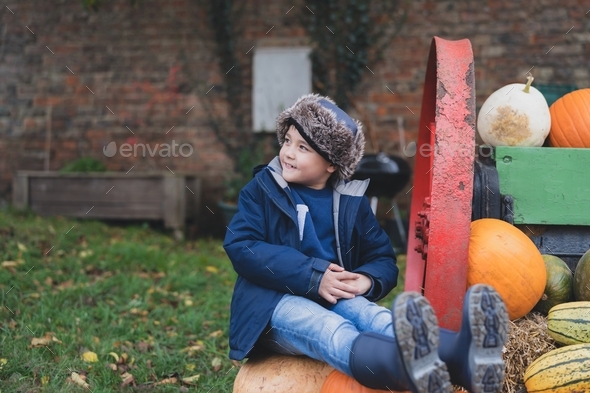 Happy kid sitting on big pumpkin patch,Cute boy having fun playing outdoor in Autumn park.