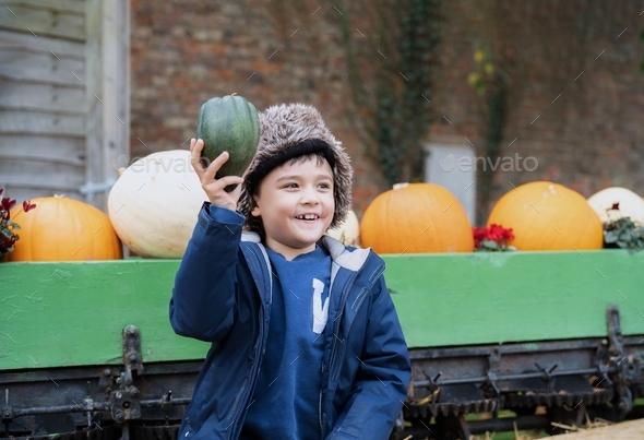 Happy kid sitting on hay patch holding pumpkin, boy having fun playing outdoor in Autumn park