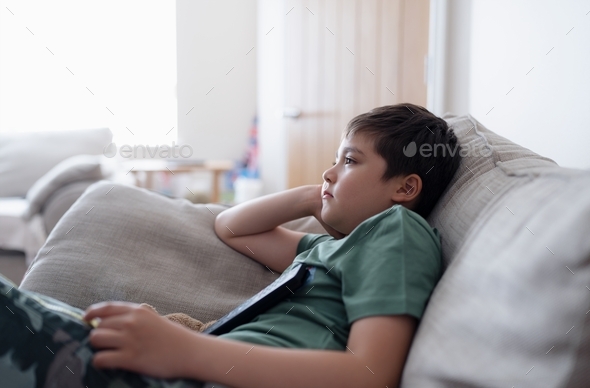 Kid with remote control and looking up with curious face,Young boy sitting on sofa watching cartoon