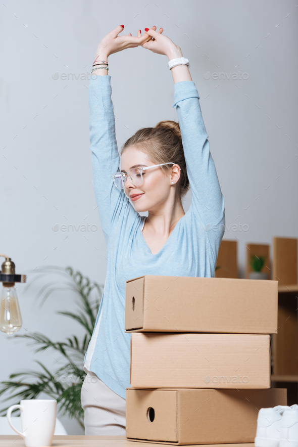 portrait of smiling tired entrepreneur stretching at workplace with cardboard boxes at home office