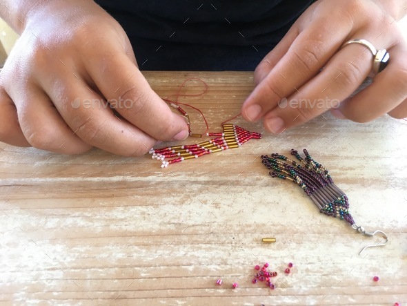 Person making beaded earrings, threading the beads