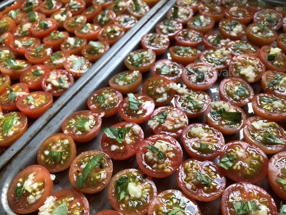 Trays of cherry tomatoes drizzled with olive oil and garnished with crushed garlic and fresh basil