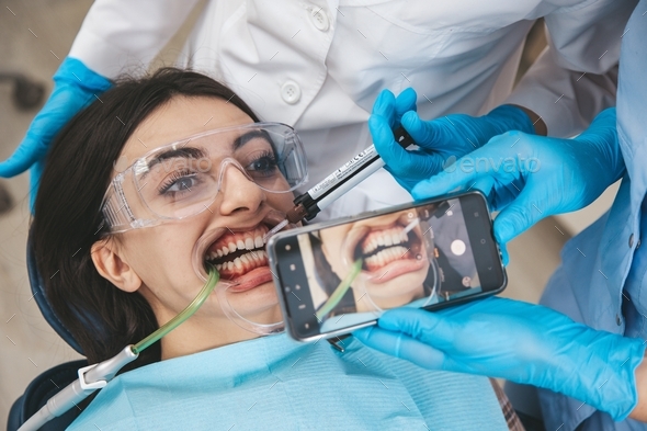 Dental care procedure at stomatology cabinet, medical assistant taking teeth photo using smartphone