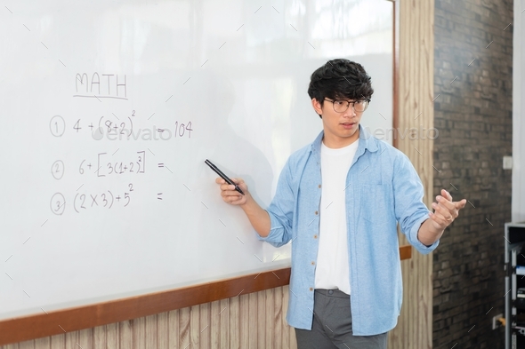 Male tutor standing in front of whiteboard and writing math equation to explaining new lesson