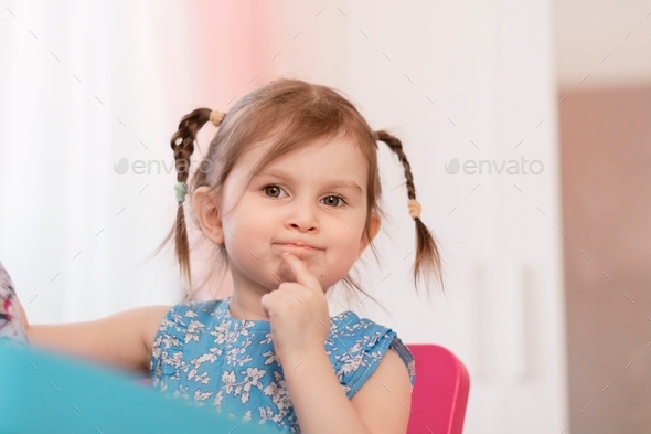 Thoughtful little brown-haired girl wearing casual blue dress touch chin with finger thinking