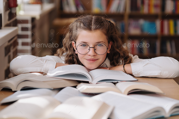 Girl studying among books sitting at the desk among books - Stock Photo - Images