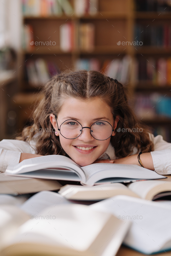 Girl studying among books sitting at the desk among books - Stock Photo - Images