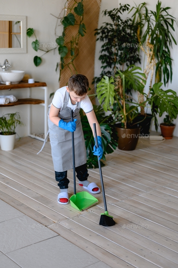 a boy in a gray apron and a white T-shirt sweeps up the garbage in his bathroom, which has flowers.
