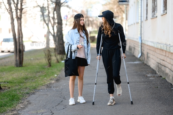 a young woman with a broken ankle walks on crutches through the city with her sister