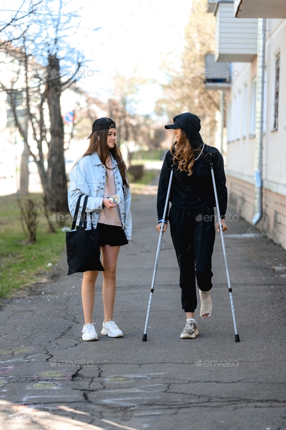 a young woman with a broken ankle walks on crutches through the city with her sister