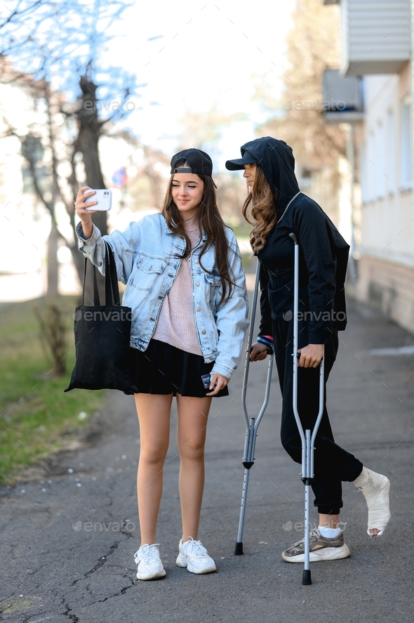 a young woman with a broken ankle walks on crutches through the city with her sister