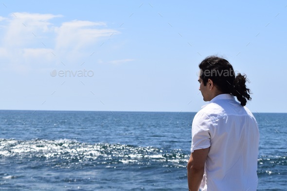 Young man gazing out at the blue sparkling ocean on a sunny day