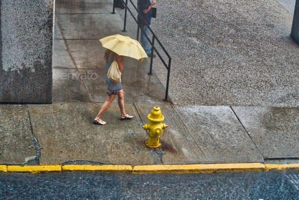 Millennial woman with a yellow umbrella walking in the pouring rain next week yellow fire hydrant