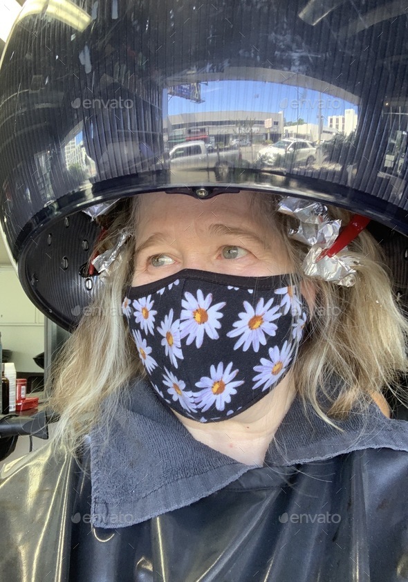 Women at hairdresser during pandemic with mask on under hairdryer Stock