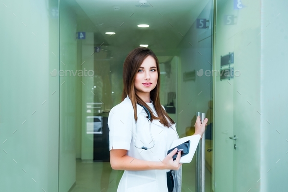 Smiling young female medical professional, doctor opening the door to her practice or hospital.