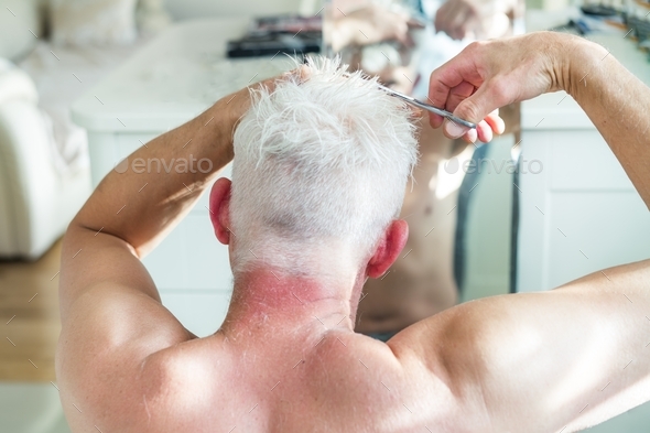 Back view man with white hair doing self haircut with scissors