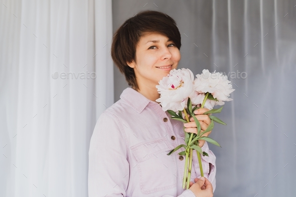 Smiling woman with light pink peony flowers on the white background.