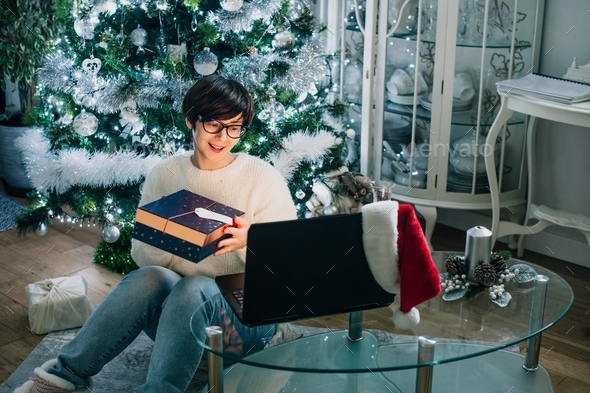 Woman holding gift box during online family greeting at home on Christmas online party