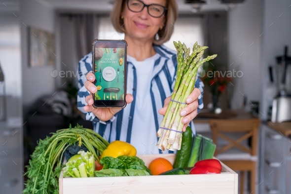 Woman holding a phone with active online mobile app of Healthy diet program and fresh asparagus