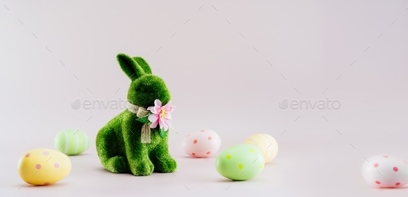 Green bunny rabbit figurine and colored easter eggs in different patterns on neutral pink background
