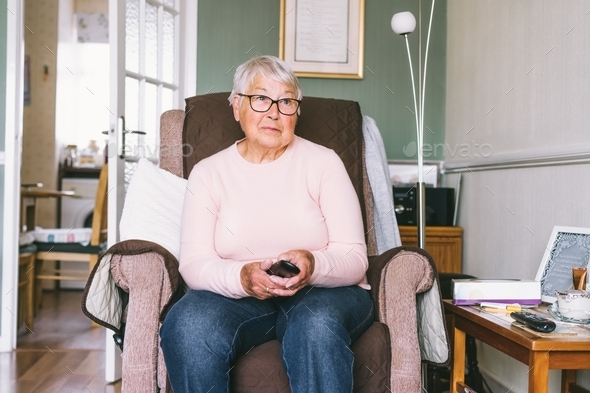 Portrait of retired elderly woman in comfortable armchair with TV remote control and watching tv