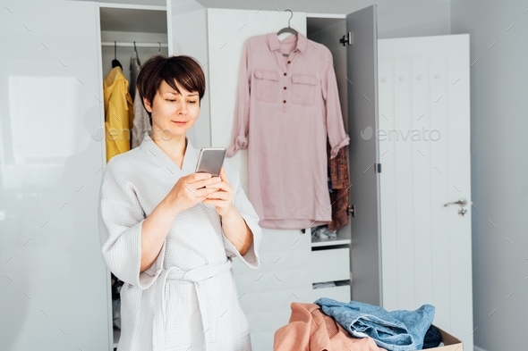 Woman using her smartphone to find places where to donate her clothes. Decluttering, Sorting clothes