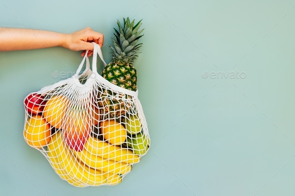 Top view female hand holding string bag, mesh bag, grocery bag with organic fresh exotic fruits
