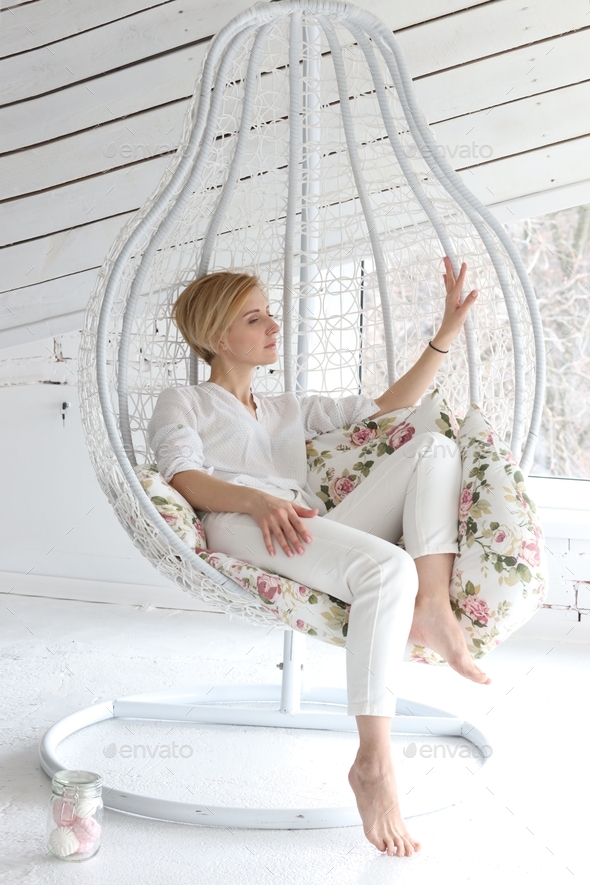 girl at a photo shoot in the studio in white clothes posing on a suspended cocoon chair