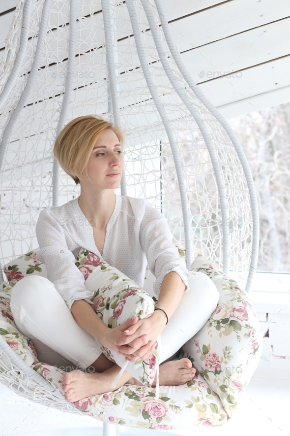 girl at a photo shoot in the studio in white clothes posing on a suspended cocoon chair