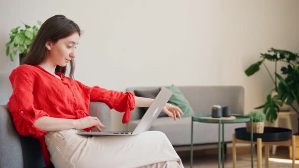 A Beautiful Young Businesswoman in a Bright Red Shirt is Typing on a Laptop alt