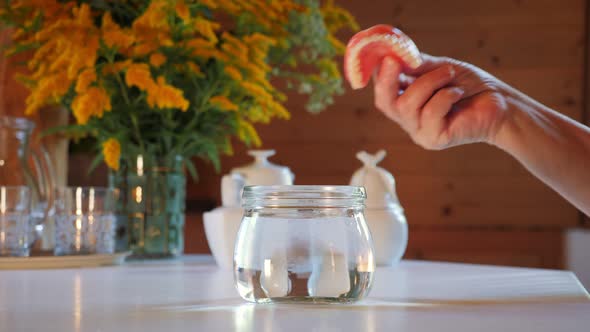 Hand taking false teeth out from glass of water alt