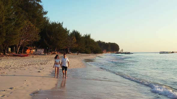 Young couple sunbathing on idyllic bay beach holiday by transparent lagoon and white sand background alt