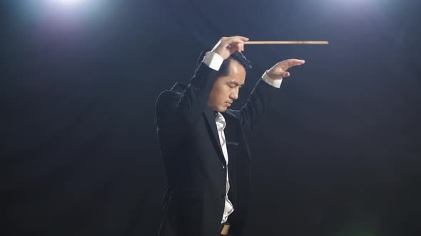 Side View Of Asian Conductor Man Holding A Baton Closing His Eyes And Showing Gesture alt