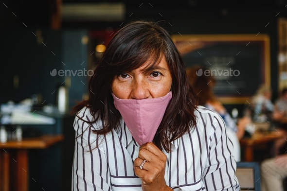 Hispanic woman pulling down her pink face mask to under nose while at a restaurant