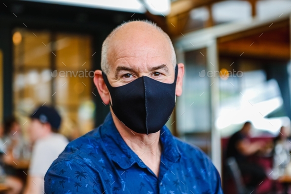 Middle aged man wearing a black face mask in a restaurant and looking at the camera