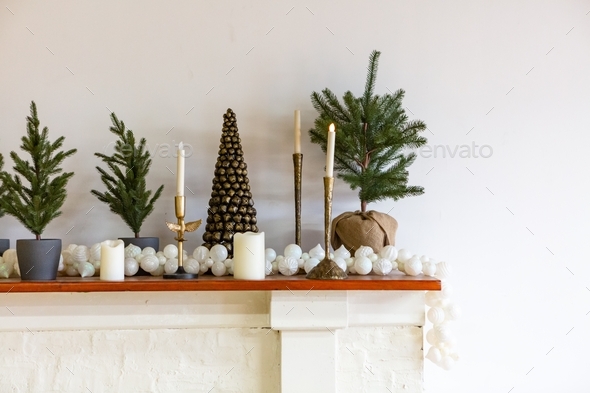 Minimalist gold holiday decorations, small Christmas trees on a fireplace mantle, white background - Stock Photo - Images