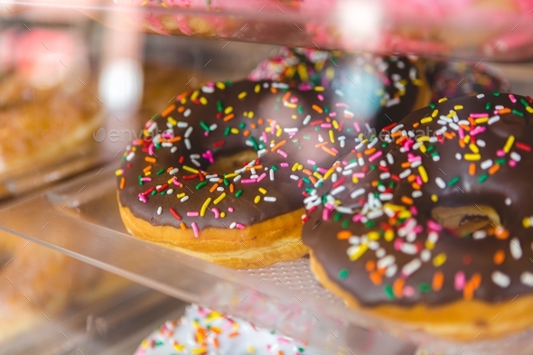 Chocolate donuts at a bakery behind glass with rainbow sprinkles - Stock Photo - Images