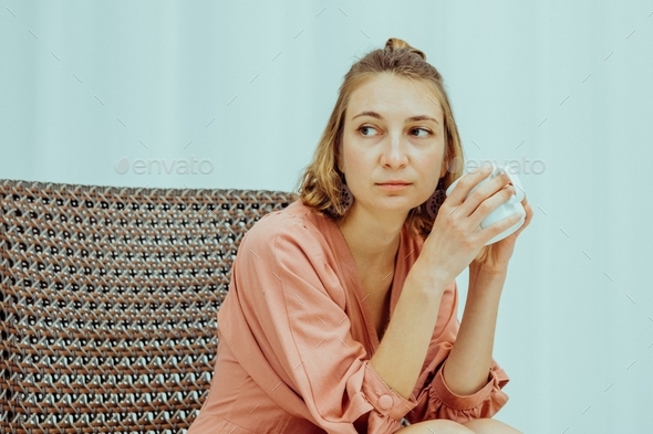 Meditative caucasian millennial woman sitting in a modern armchair drinking hot coffee or tea.