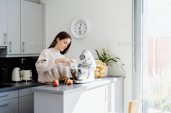 Teenager girl using mixer or food processor making dough. Child cooking at modern kitchen