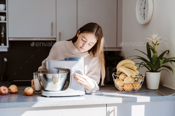 Teenager girl using mixer or food processor making dough. Child cooking at modern kitchen