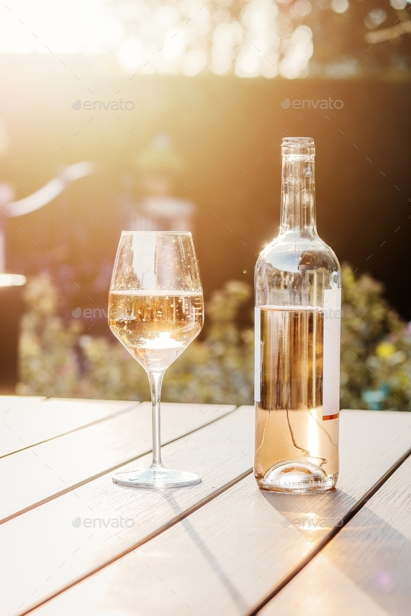 Cold rose wine in bottle and glass on table in garden at sunset light