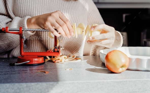 Close up of girl hands slicing apple using peeler corer slicer machine. Child cooking charlotte pie