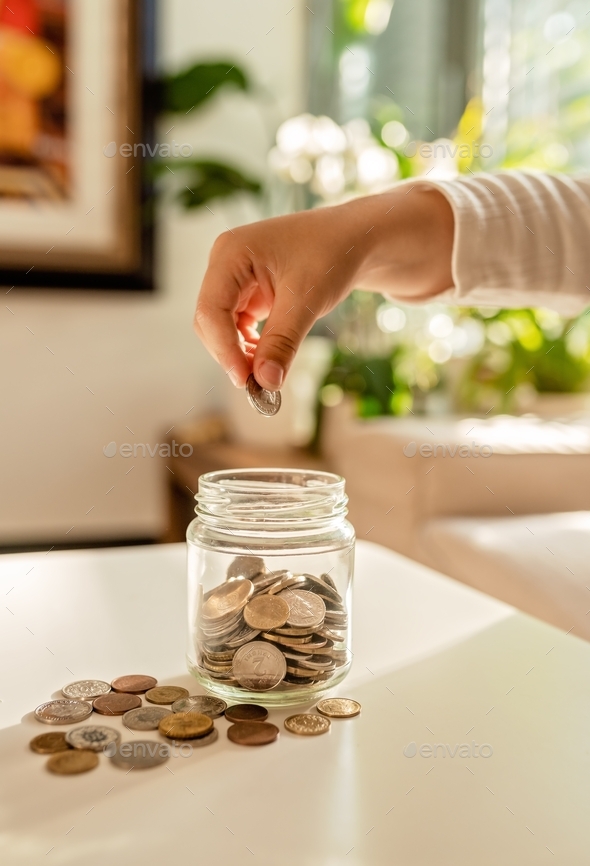 Hand of little child putting coin into glass jar. Kid counting his money saving from change