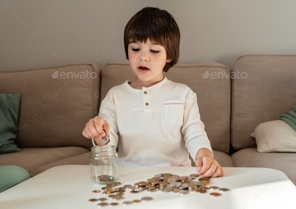 Little child putting coins into glass jar. Kid counting his money saving from change